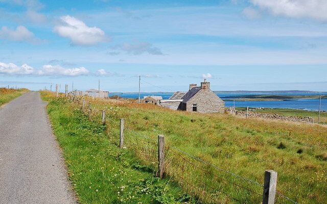 A rural road with a stone house and a view of the sea.