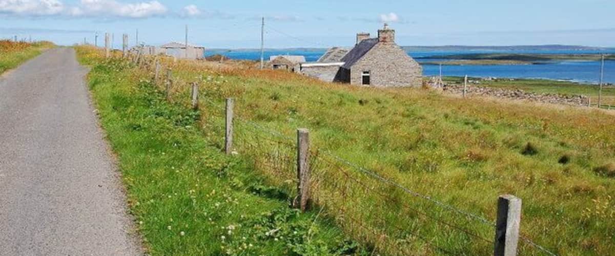 A rural road with a stone house and a view of the sea.