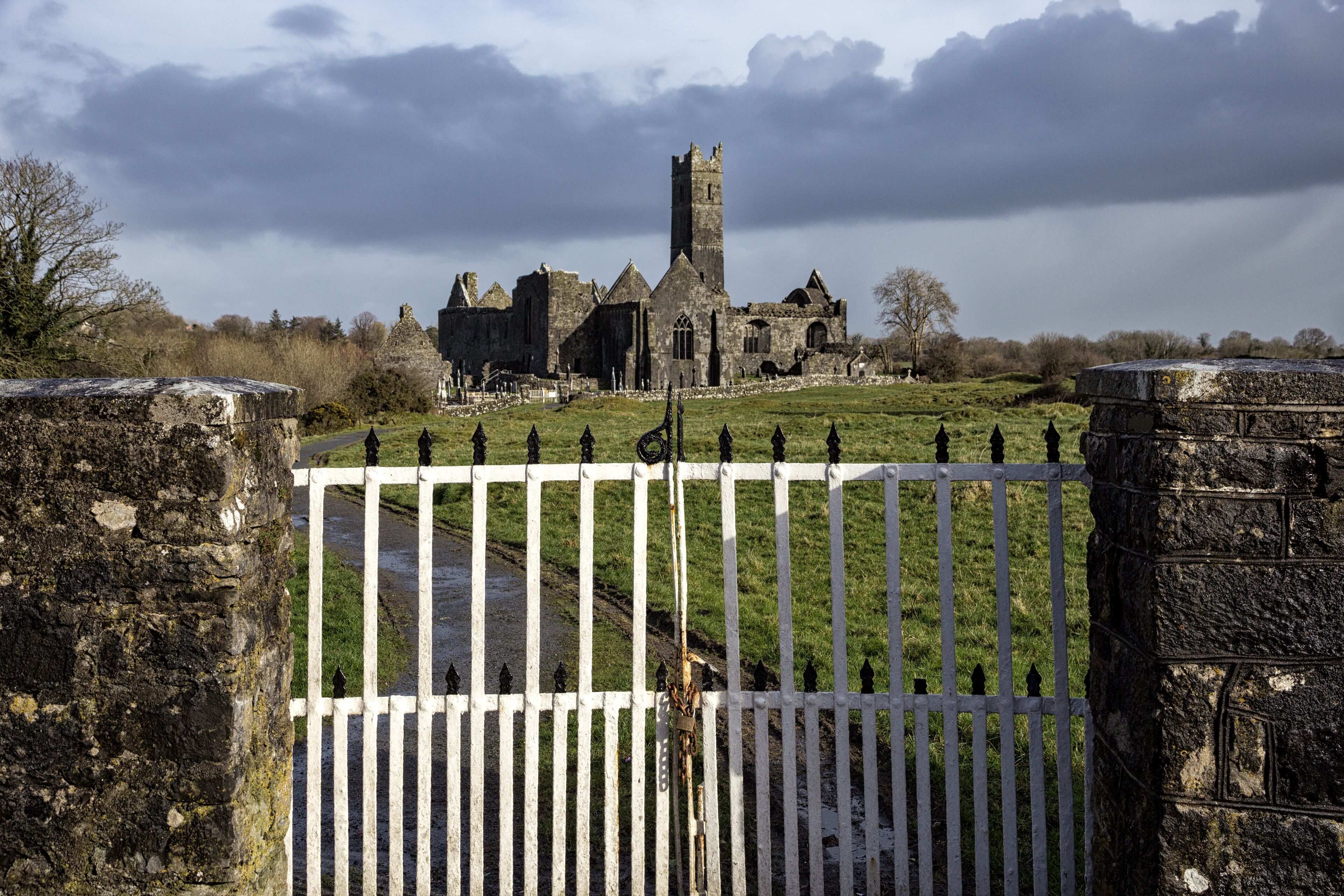 A historic stone church with a tall tower, surrounded by a white fence and a stone wall.