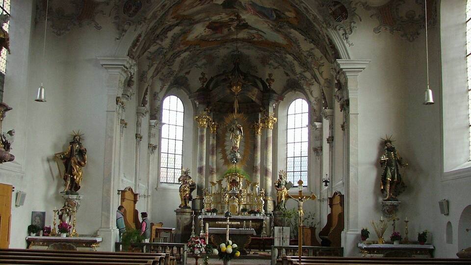 An ornate church interior with arched ceilings, a central altar, and religious statues.