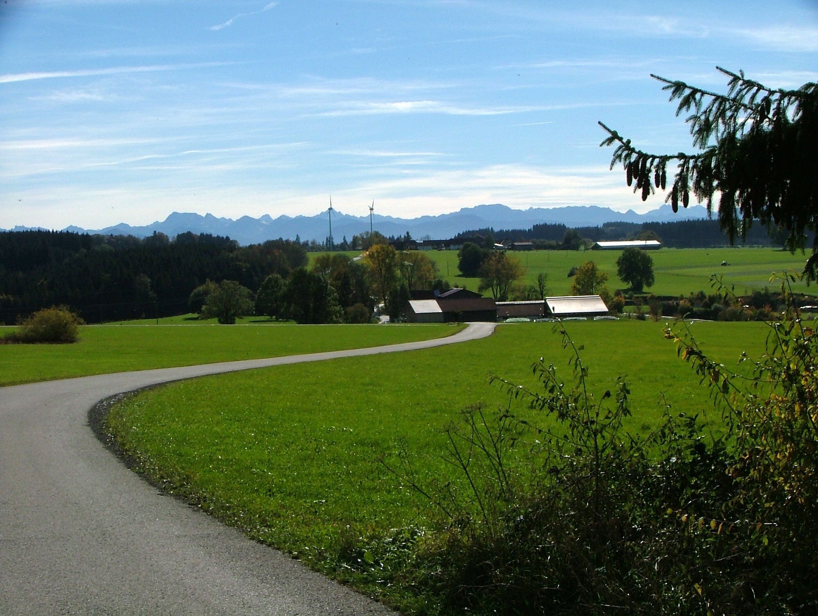 A winding road through a green landscape with mountains in the background.