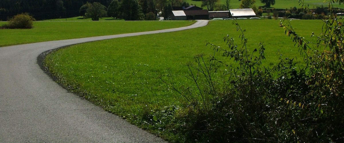 A winding road through a green landscape with mountains in the background.