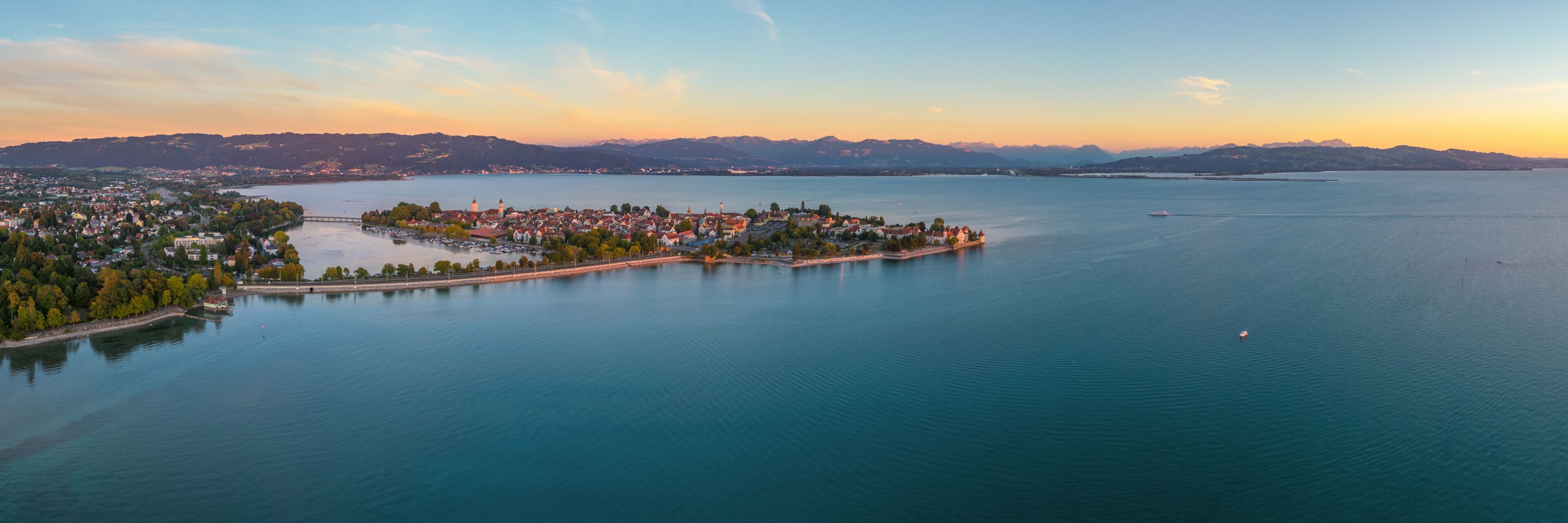 A coastal town with a central island, surrounded by calm waters and distant mountains.