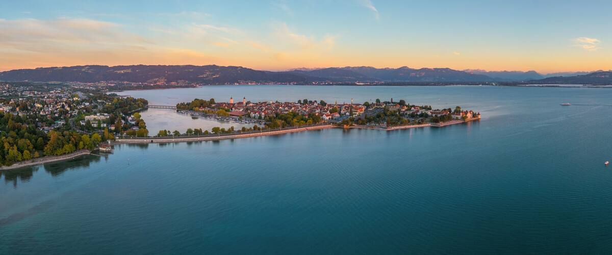 A coastal town with a central island, surrounded by calm waters and distant mountains.