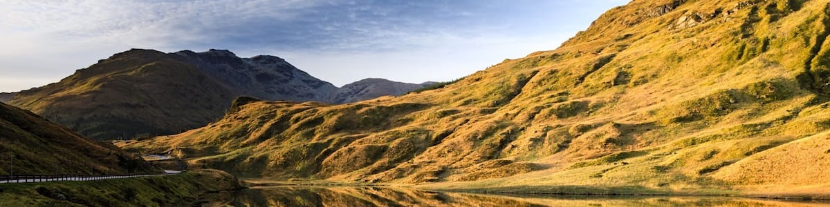 Un paysage montagneux avec une vallée, un petit lac et une route.