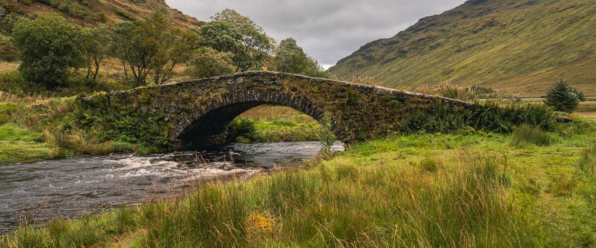 A stone bridge over a river in a hilly landscape.