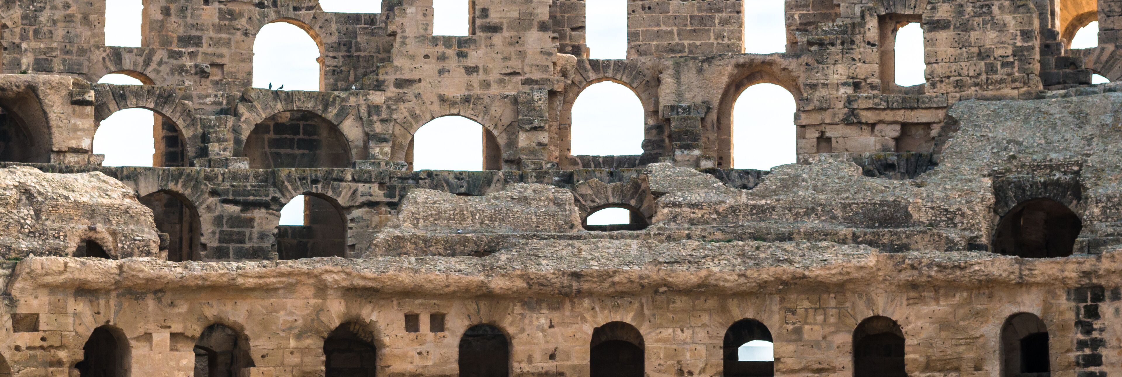 An ancient stone structure with multiple arched openings and a rough, eroded surface.