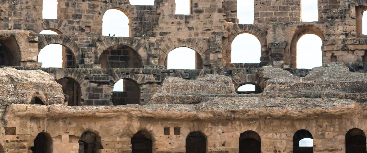 An ancient stone structure with multiple arched openings and a rough, eroded surface.