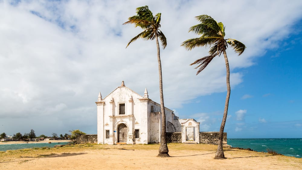 Church and fortress of San Antonio on Mozambique island, with two palm trees on sand. Indian ocean coast, Nampula province, Mozambique. Fortim de Santo António na Ilha de Moçambique.