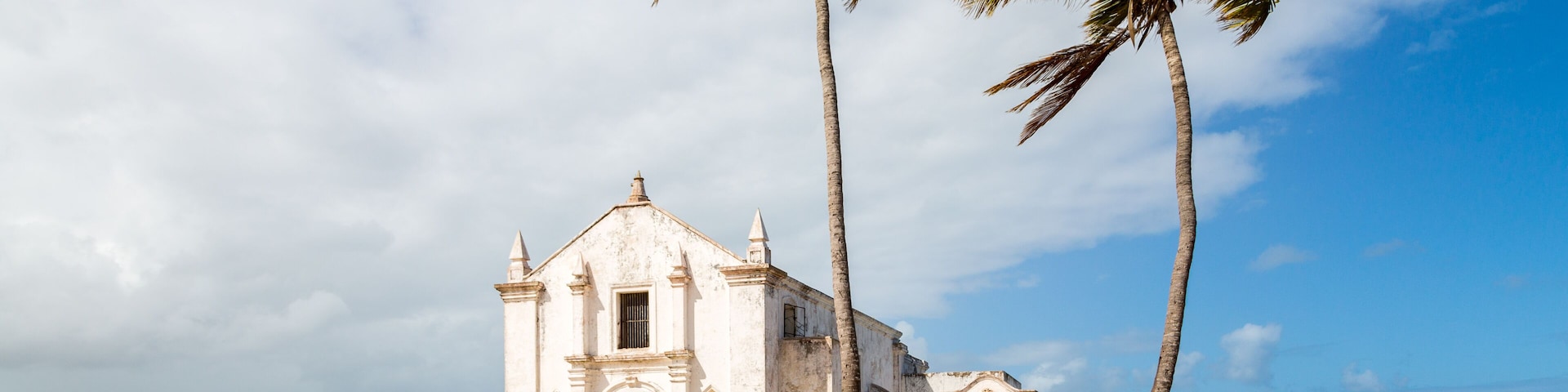 Church and fortress of San Antonio on Mozambique island, with two palm trees on sand. Indian ocean coast, Nampula province, Mozambique. Fortim de Santo António na Ilha de Moçambique.