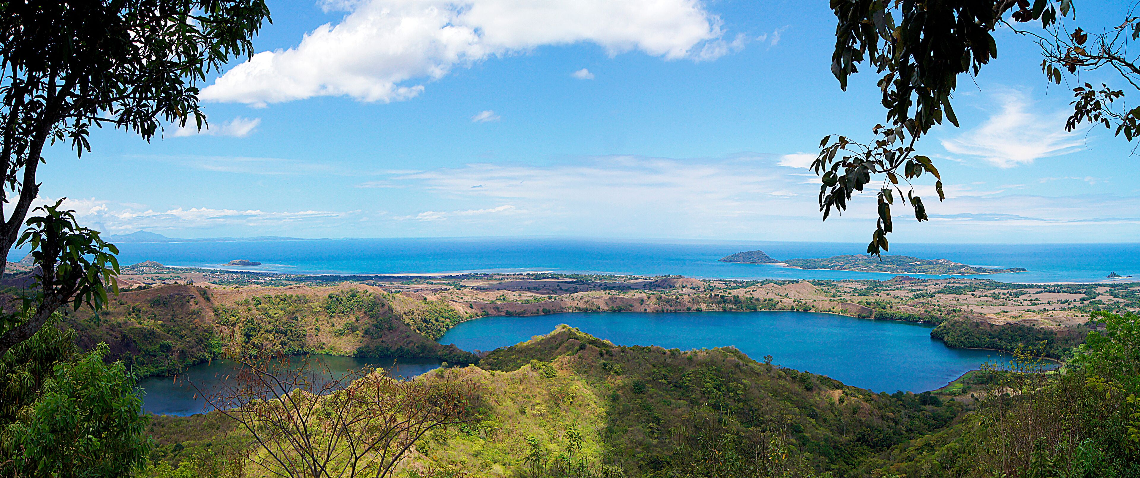 A coastal landscape with a large body of water, green hills, and a clear blue sky.