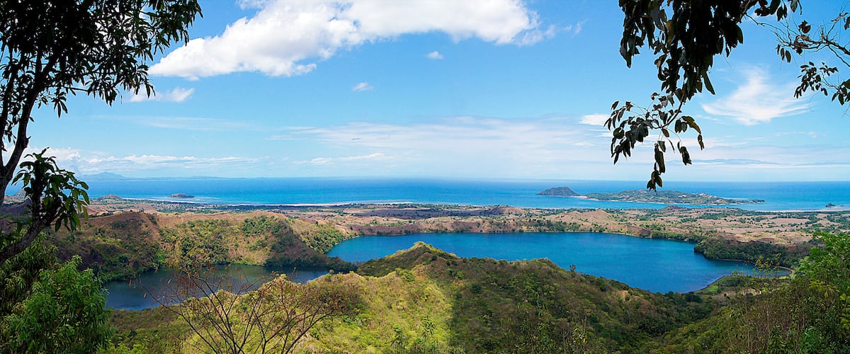 A coastal landscape with a large body of water, green hills, and a clear blue sky.