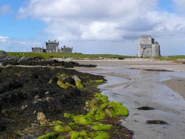 A coastal landscape with rocky shores, green moss, and two historic stone buildings.