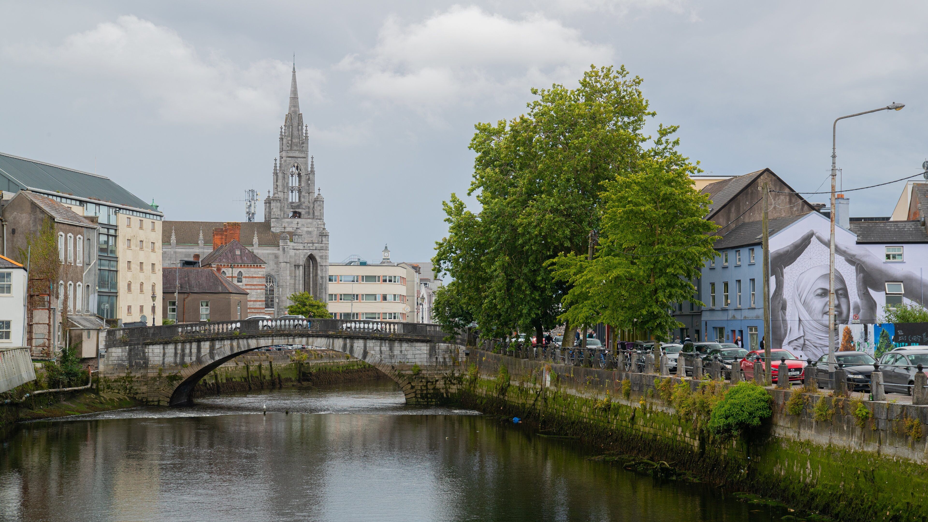 A stone bridge over a river, a church tower, and a tree-lined street.