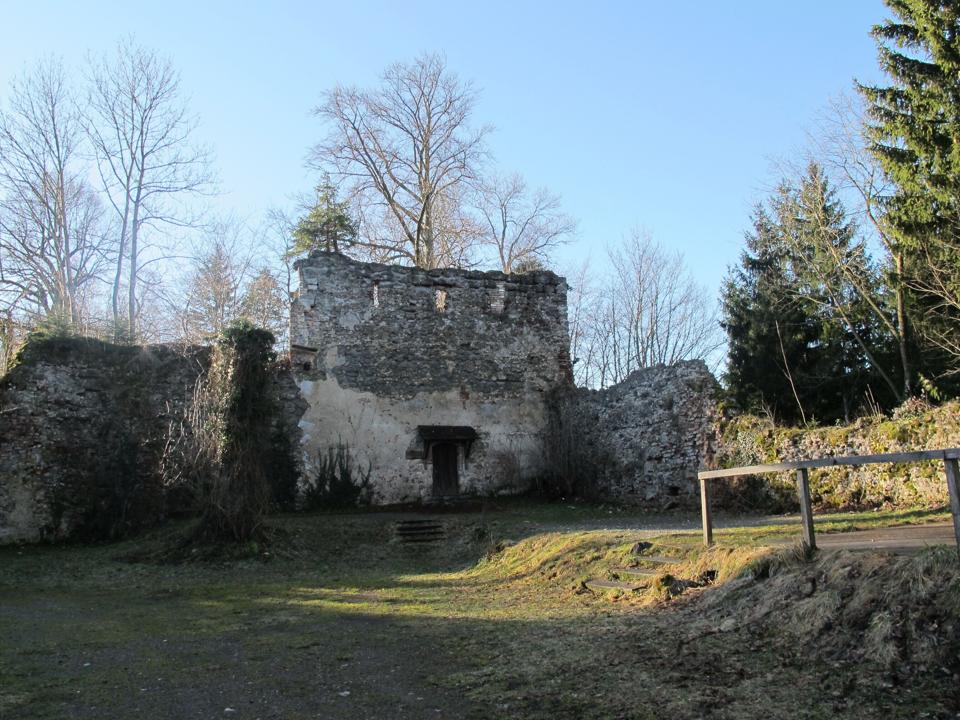 An old stone building with a wooden door, surrounded by trees and a grassy area.