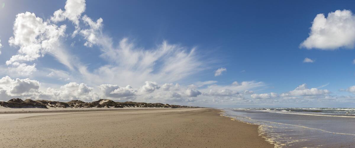 A beach with sand dunes and waves in the background.