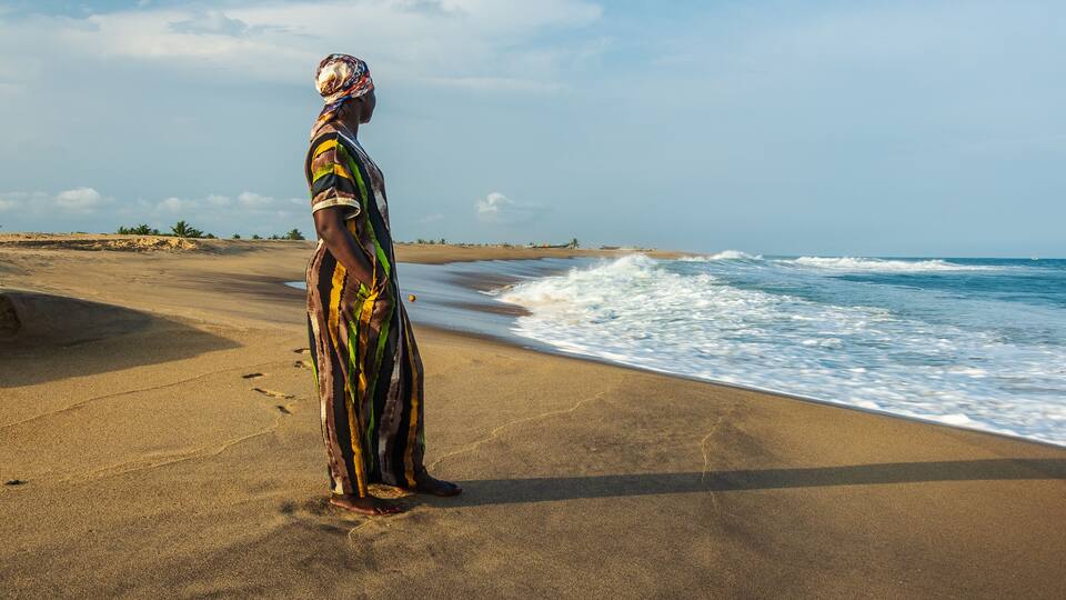 A person standing on a sandy beach with waves crashing onto the shore.