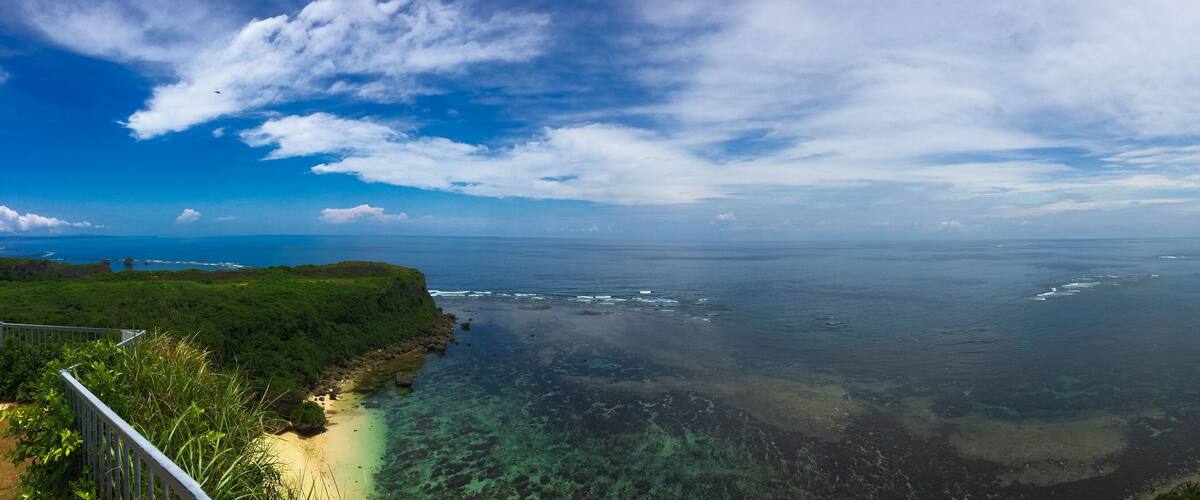 A coastal landscape with a clear sky, a sandy beach, and a rocky shoreline.