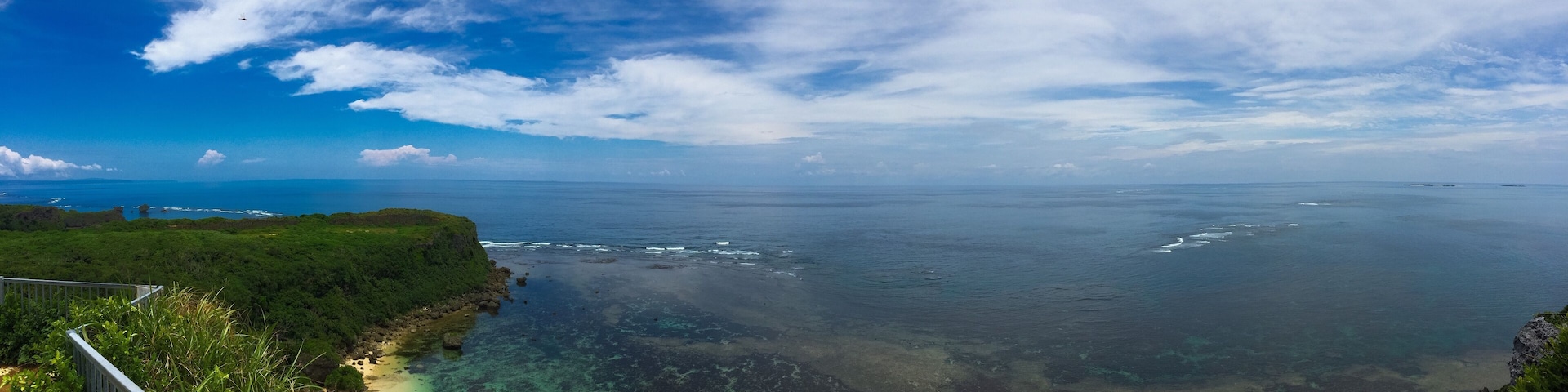 A coastal landscape with a clear sky, a sandy beach, and a rocky shoreline.