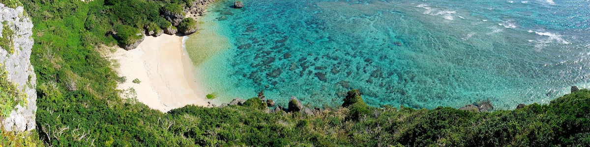 A coastal landscape with a clear turquoise sea, a sandy beach, and lush green vegetation.