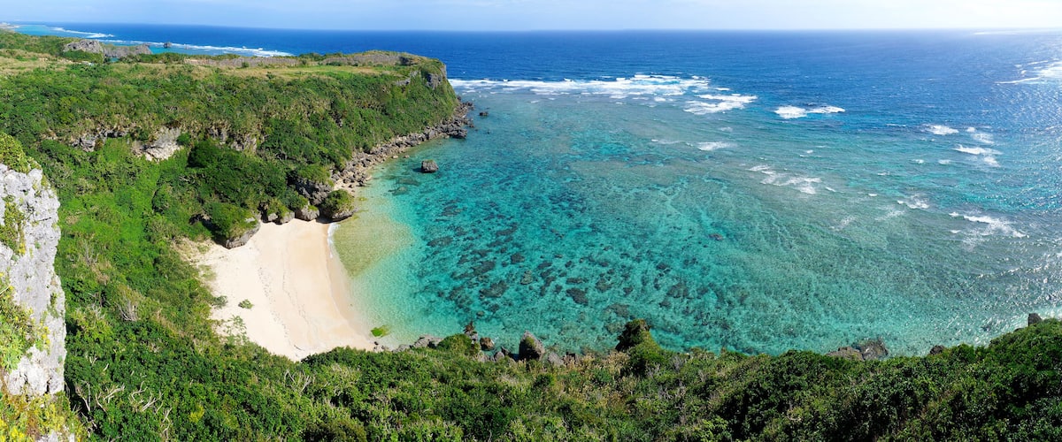 Un paisaje costero con un mar turquesa transparente, una playa arenosa y una vegetación verde exuberante.