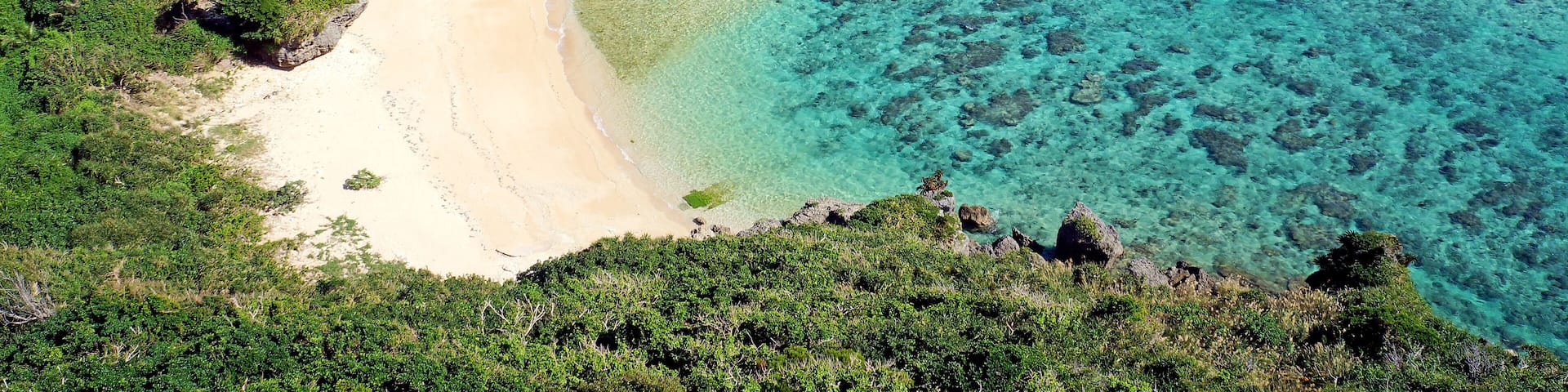 A coastal landscape with a sandy beach, clear turquoise waters, and lush green vegetation.