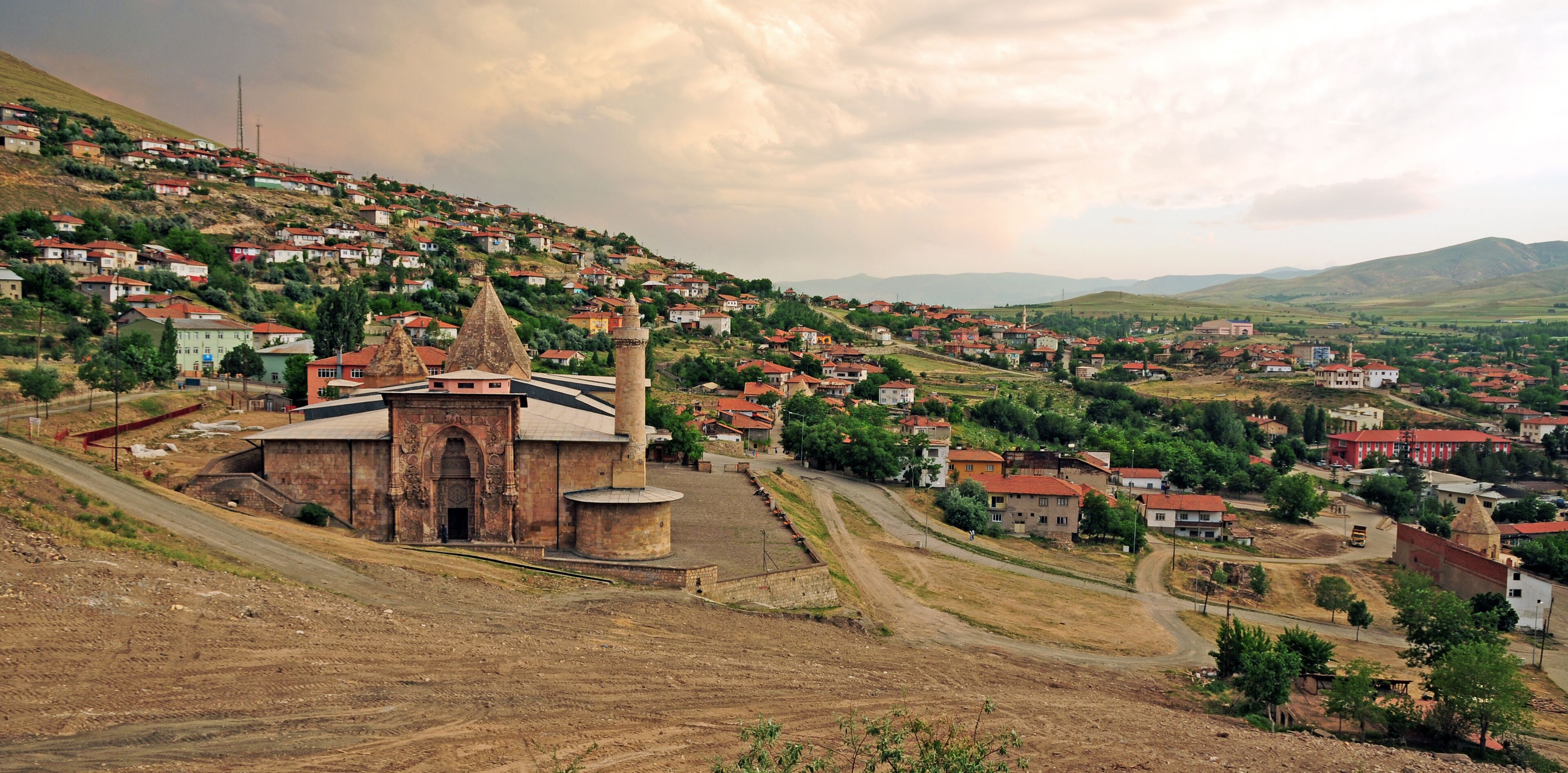 A hillside village with a prominent church, terraced houses, and rolling hills in the background.