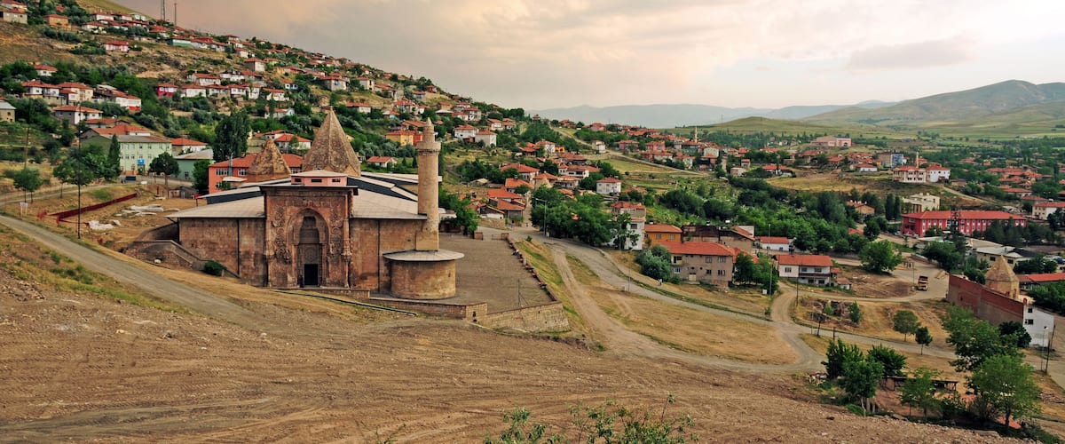 A hillside village with a prominent church, terraced houses, and rolling hills in the background.