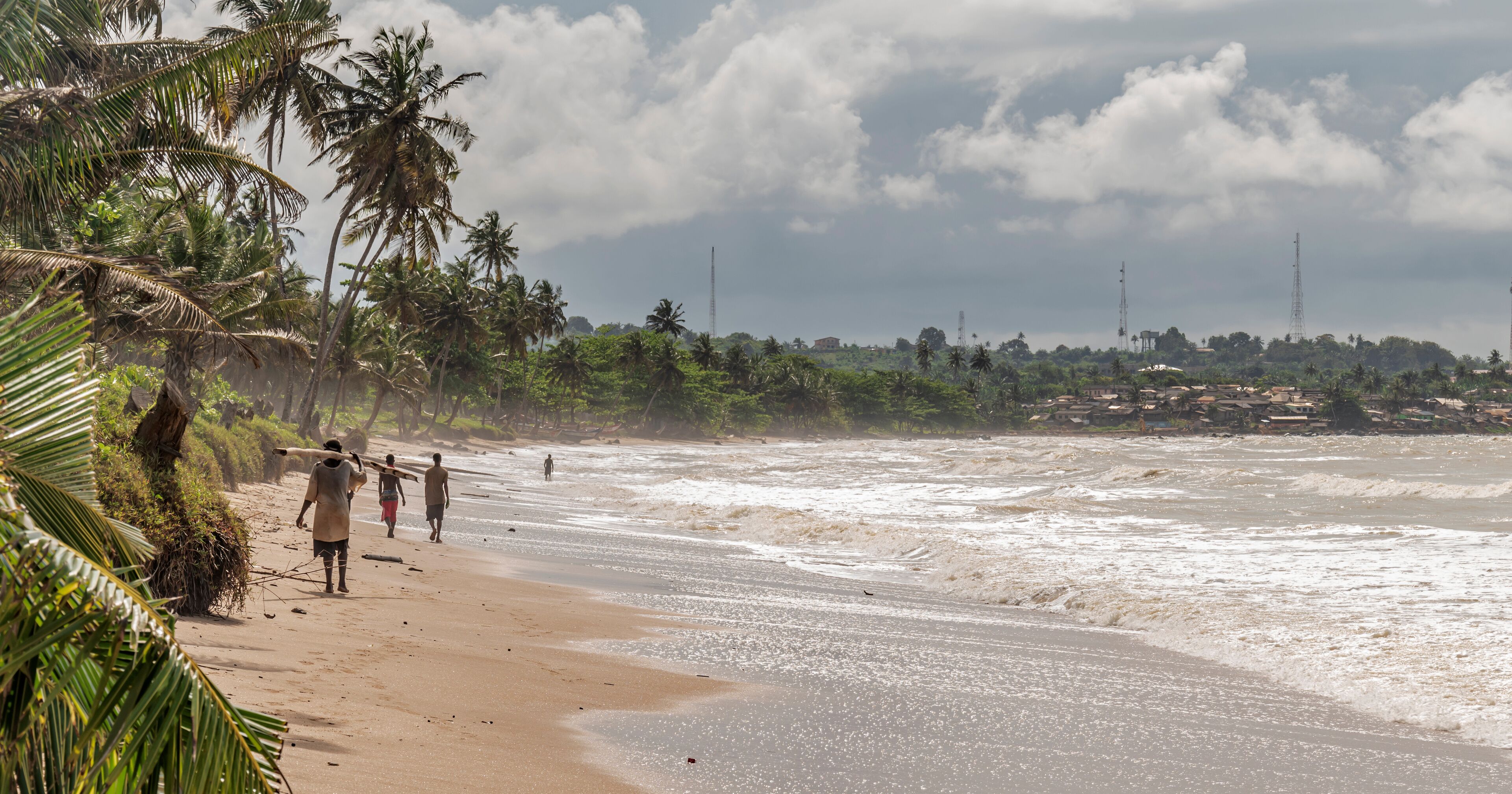 The fishing people walk on the African gold coast where the sea is colored by the sand. Axim beach is located in Ghana West Africa.