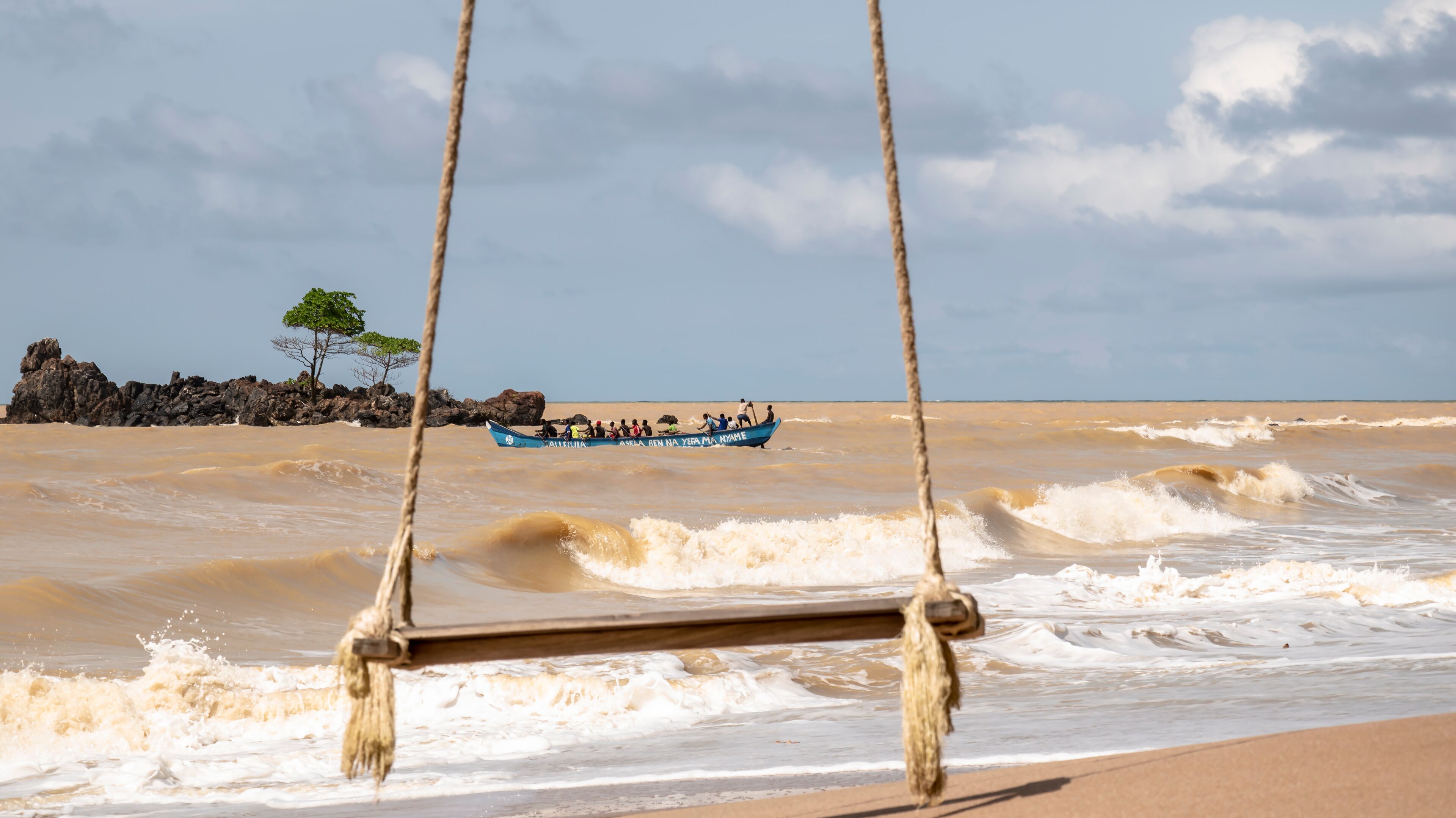 A hanging swing on an empty beach with a fishing boat in the background on the way out and the fishing spot is Axim Ghana West Africa.