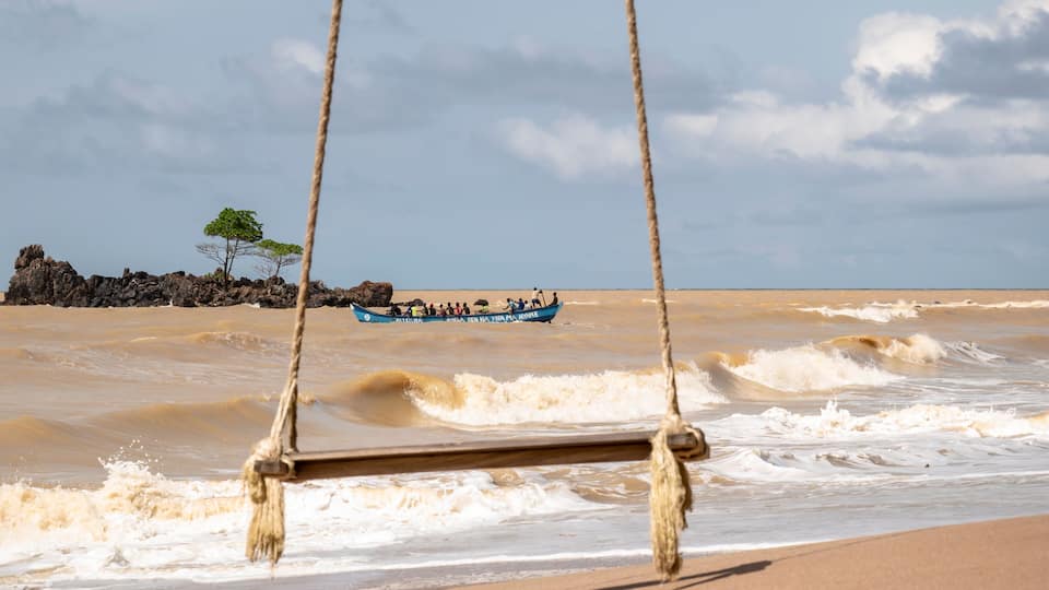 A wooden swing overlooking a turbulent river with a boat in the distance.