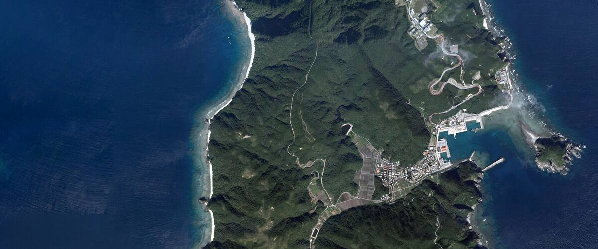 A coastal region with a narrow landmass surrounded by deep blue waters, featuring a rugged coastline and a dense green forested area.