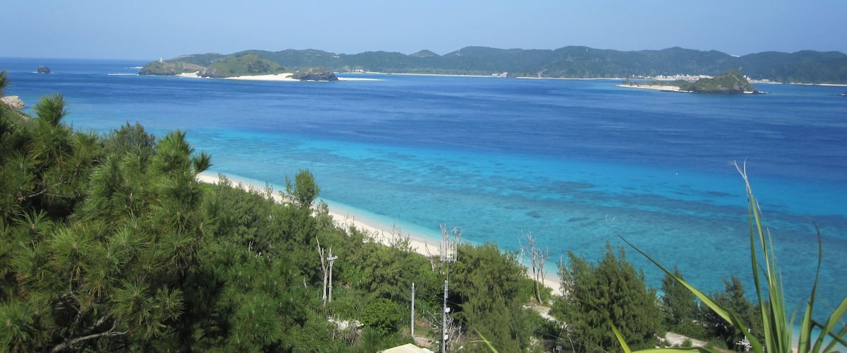 A coastal landscape with clear blue waters, sandy beaches, and green hills in the background.