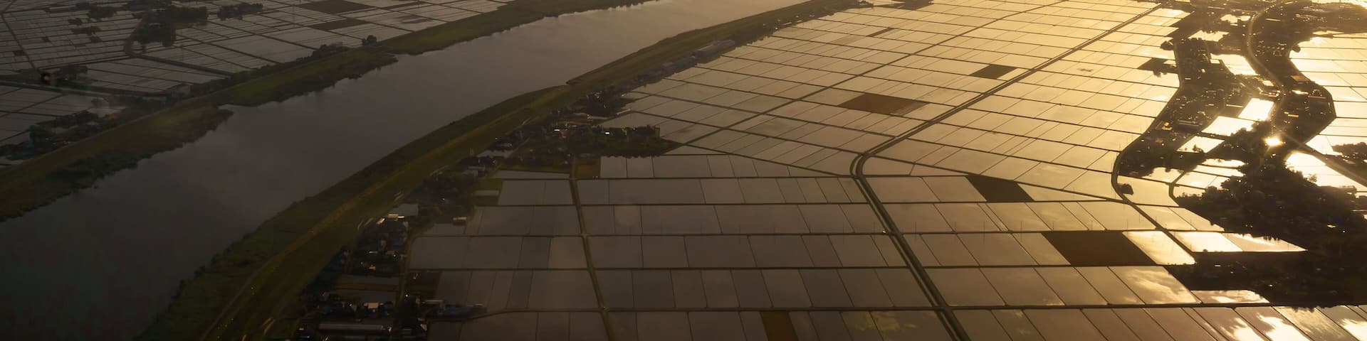 An aerial view of a river winding through agricultural fields during sunrise.