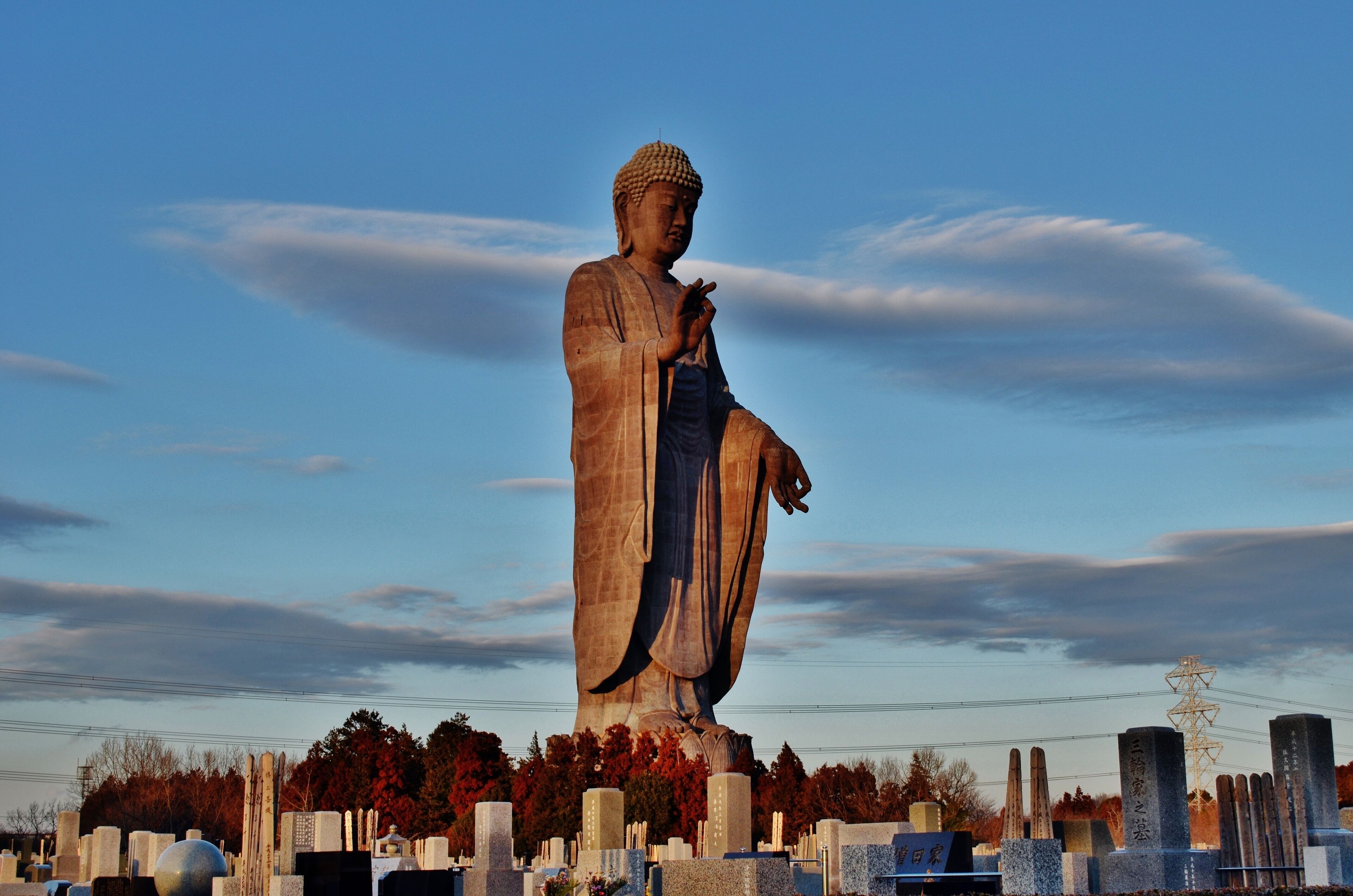 A large Buddha statue in a cemetery with autumn trees in the background.