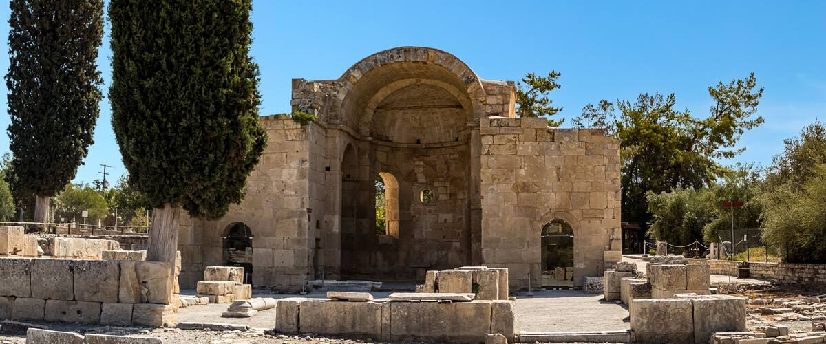 An ancient stone structure with an arched entrance, surrounded by stone blocks and tall trees.