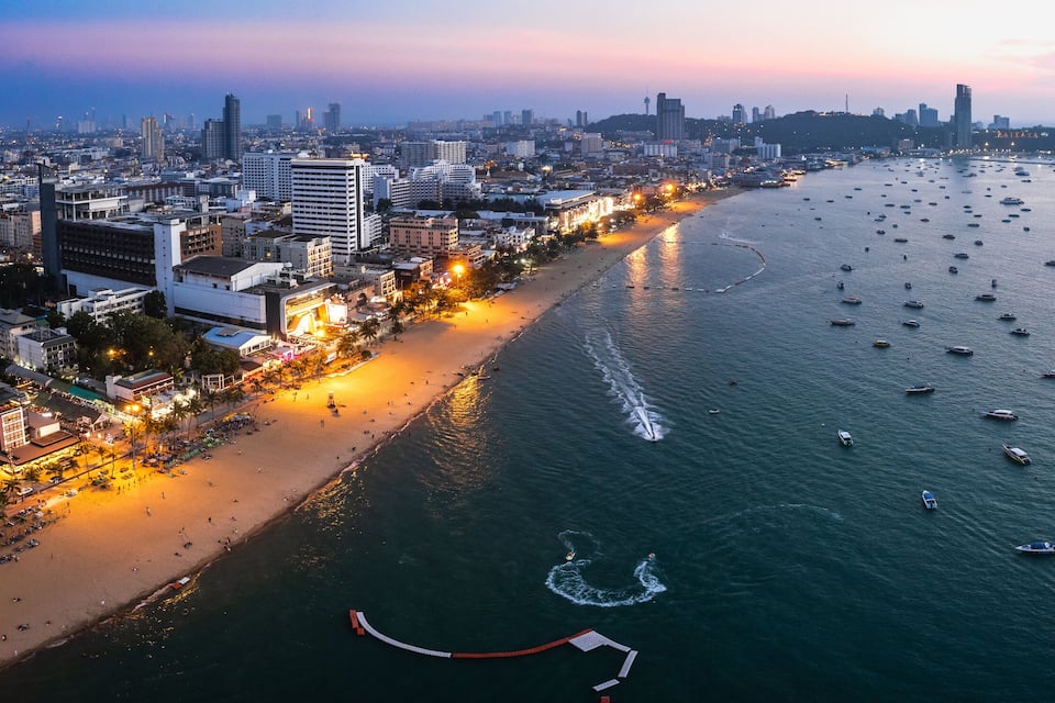 A coastal cityscape with a beach, numerous boats, and a skyline of high-rise buildings.