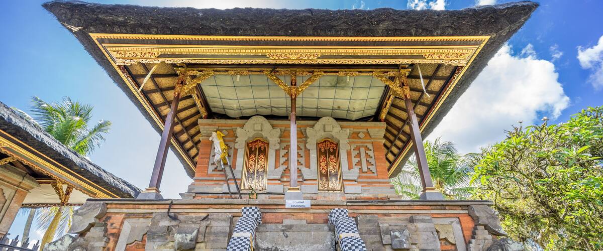 A traditional Balinese temple with ornate carvings, a checkered stone staircase, and a thatched roof.