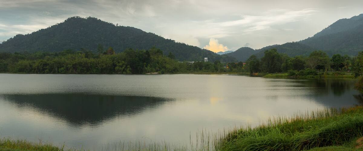 A calm lake surrounded by lush green hills and a cloudy sky.