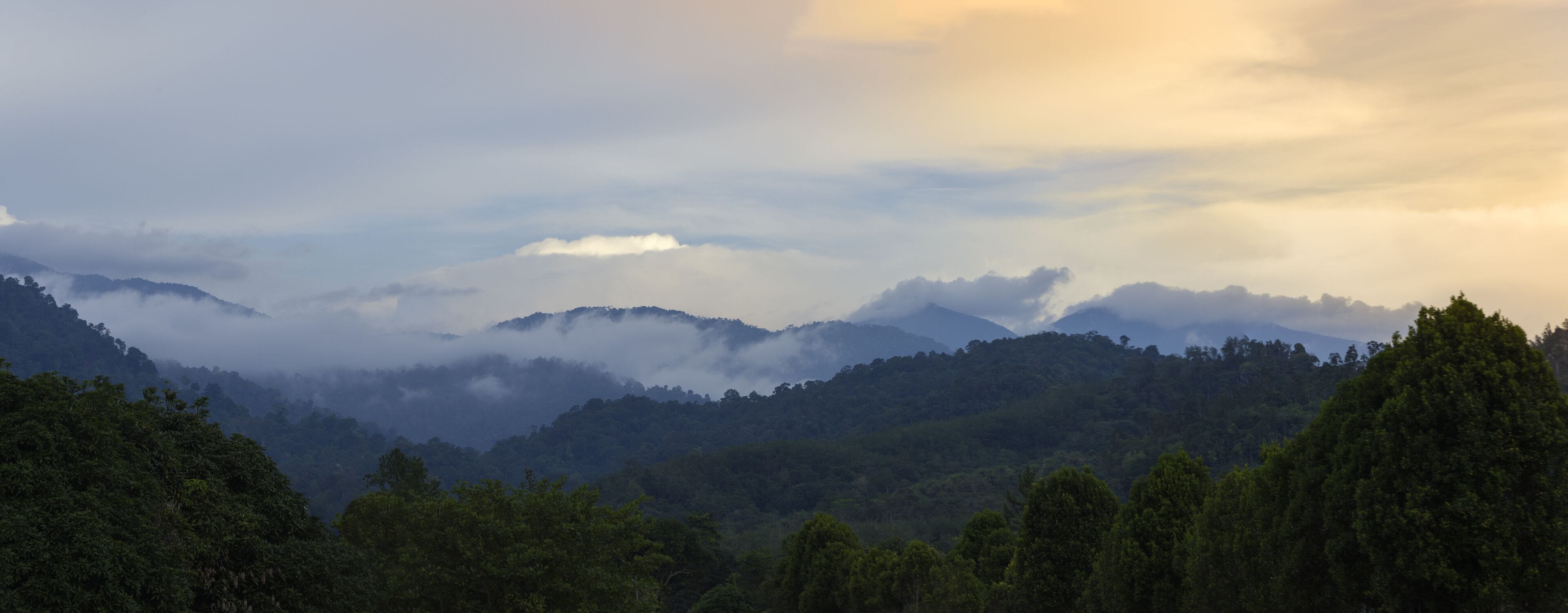 the mountains of BANJARAN TITIWANGSA surrounded by white clouds near the sunset