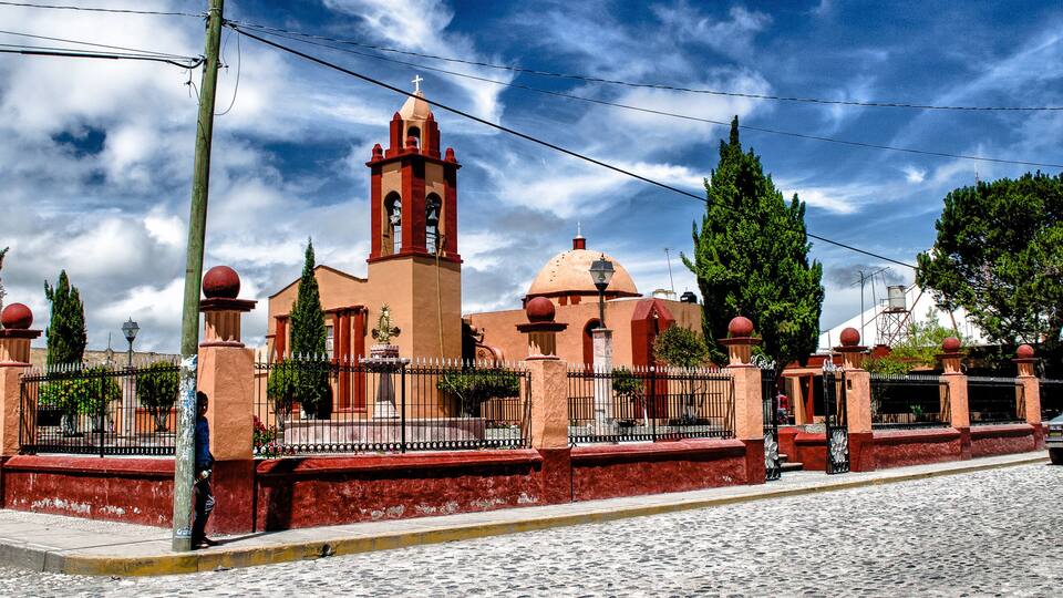 A historic church with a bell tower, surrounded by a cobblestone street and a metal fence.