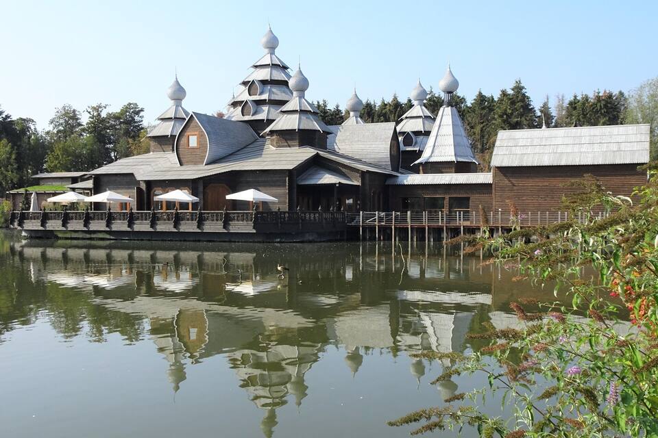 A traditional wooden building with multiple domed roofs by a calm body of water.