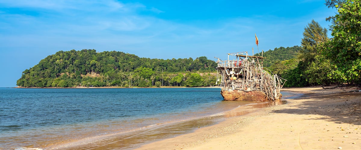 A sandy beach with a wooden structure on the shore and a forested island in the background.