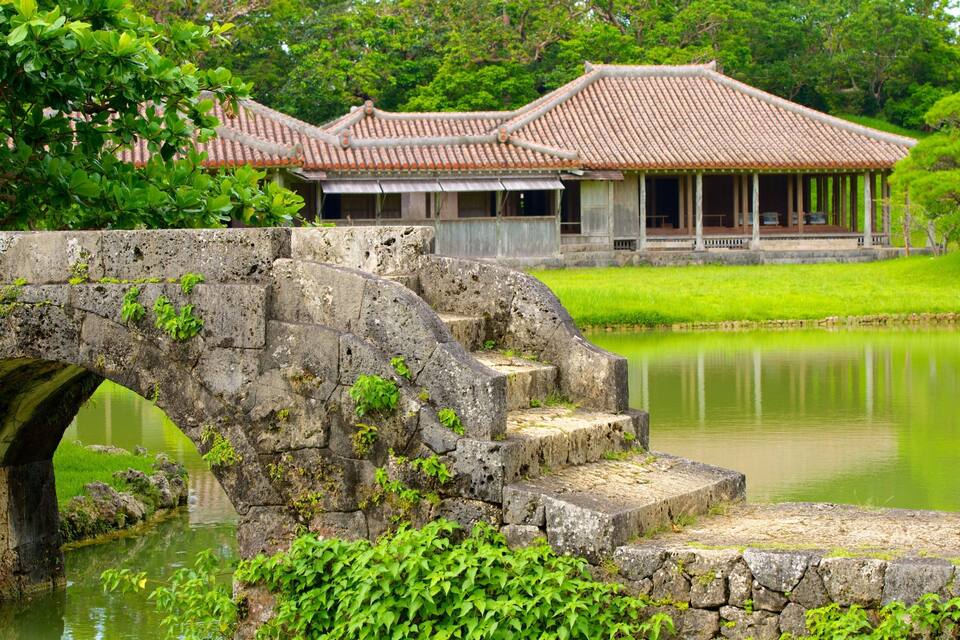 A stone bridge over a pond, traditional buildings, and lush greenery.