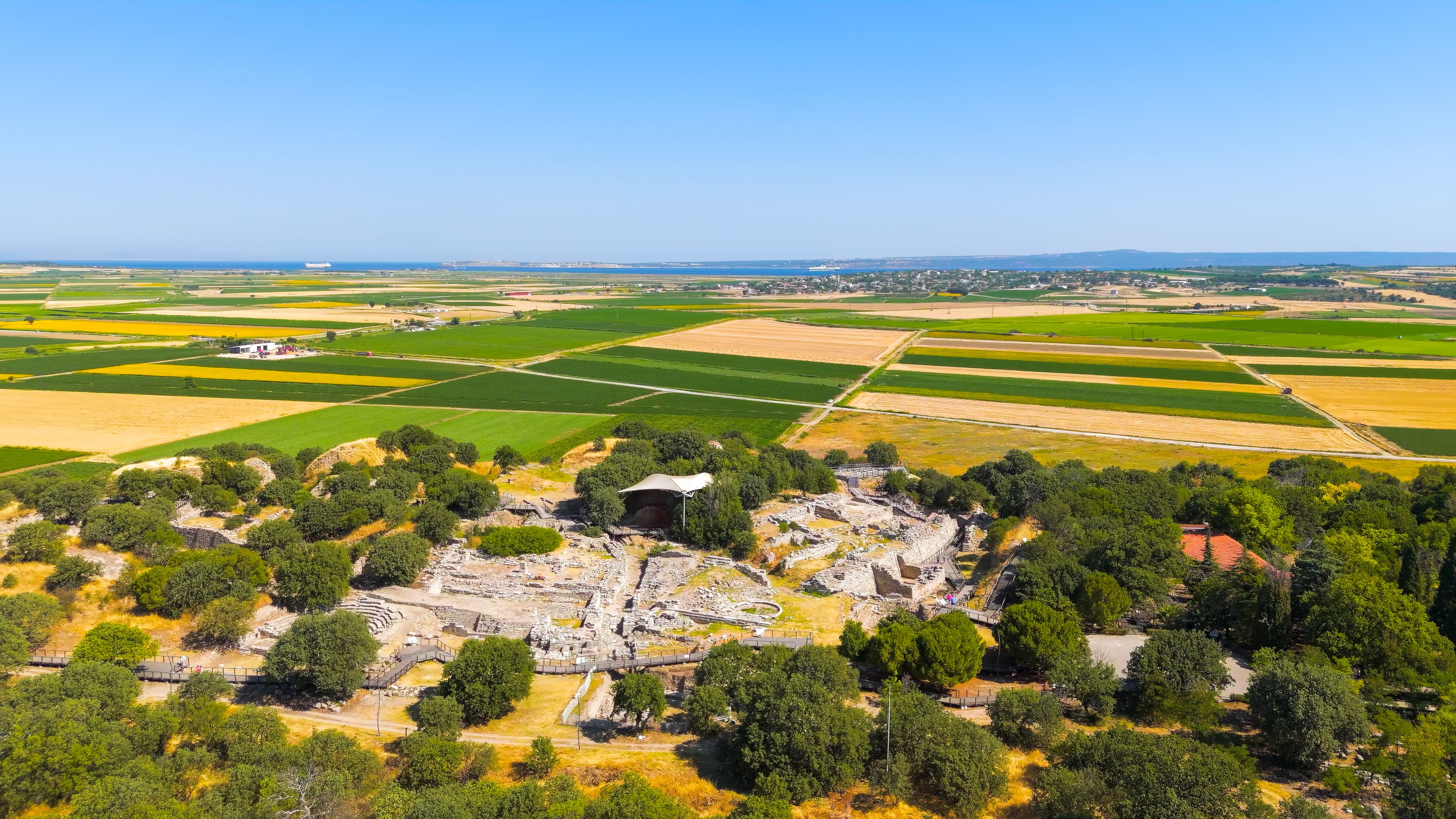 An aerial view of a historical site with ruins, surrounded by agricultural fields and a clear sky.