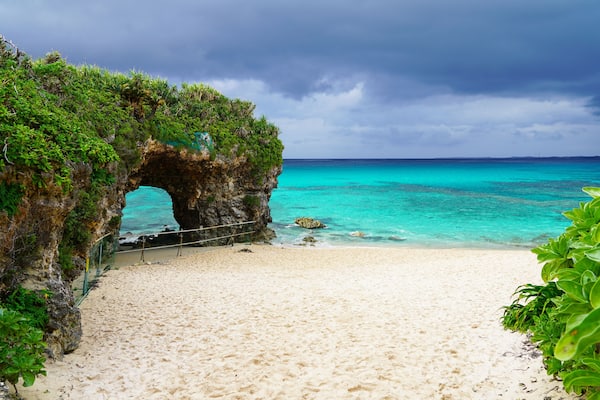 Travel to famous Paradise beach of Sunayama on Miyako Island in Japan. Seascape against blue stormy sky before rain, bright birch water, snow-white sand and a stone cliff overgrown with greenery
