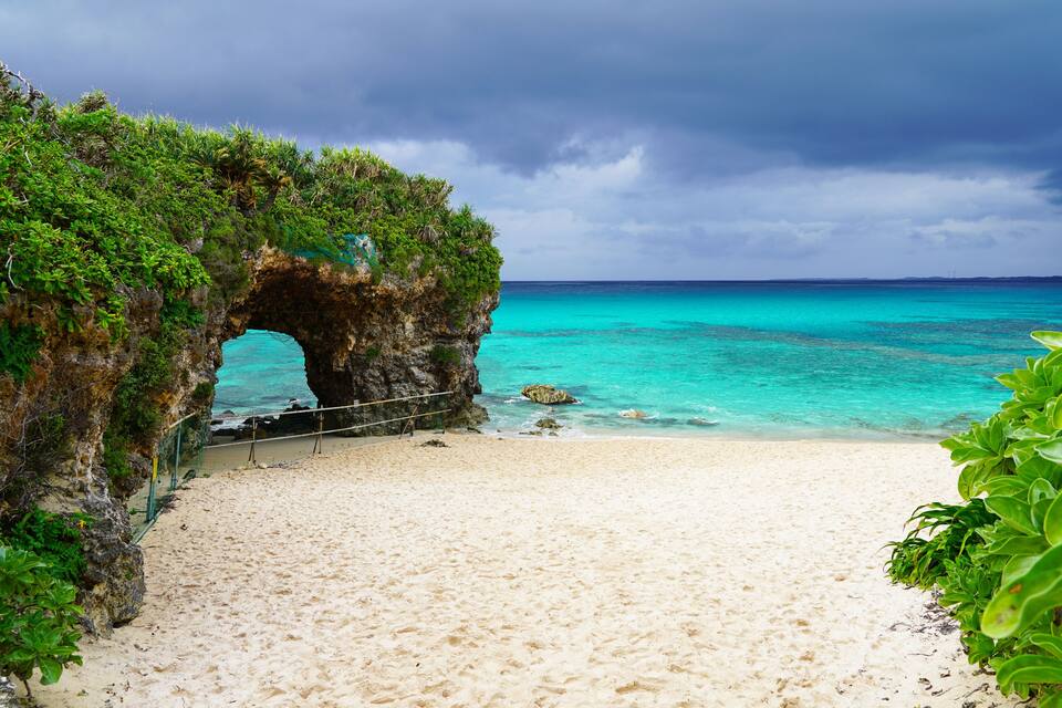 A beach with a natural rock arch, clear turquoise waters, and lush greenery.