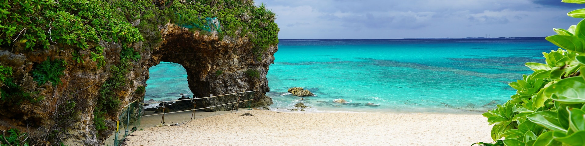 Travel to famous Paradise beach of Sunayama on Miyako Island in Japan. Seascape against blue stormy sky before rain, bright birch water, snow-white sand and a stone cliff overgrown with greenery