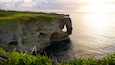 Un paysage côtier caractérisé par une formation rocheuse imposante, avec une arche naturelle qui s’étend au-dessus de la mer.