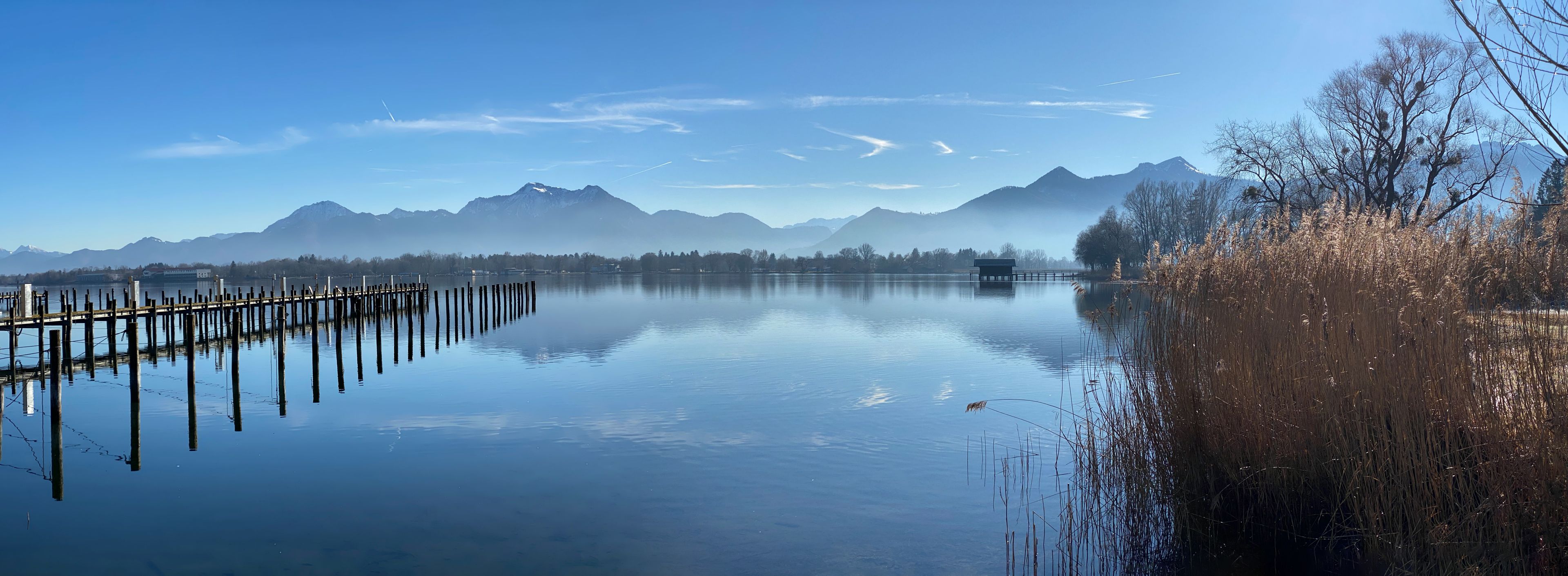 A calm lake with a wooden dock extending into the water, surrounded by mountains and sparse trees.